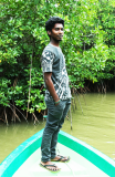 Sakthivel Kishorekumar  standing on the prow of a boat on the water with overhanging trees behind